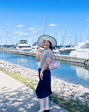 Load image into Gallery viewer, Woman standing by a marina with boats and a clear blue sky.