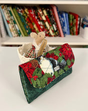 Load image into Gallery viewer, Quilted fabric wallet with Christmas design on a white surface, with a bookshelf in the background.