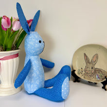 Load image into Gallery viewer, Blue plush toy rabbit next to a potted plant and a decorative plate with a rabbit design on a white surface.