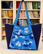 Load image into Gallery viewer, Blue floral tote bag on a table with a bookshelf in the background
