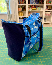 Load image into Gallery viewer, Blue tote bag with floral pattern on a green cutting mat in front of a bookshelf.
