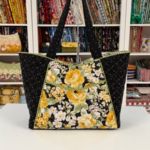 Load image into Gallery viewer, Floral tote bag with black quilted handles in front of a bookshelf with fabric samples.
