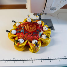 Load image into Gallery viewer, Silk Pincushion Decorative item with gold and red elements on a sewing machine with a ruler below.
